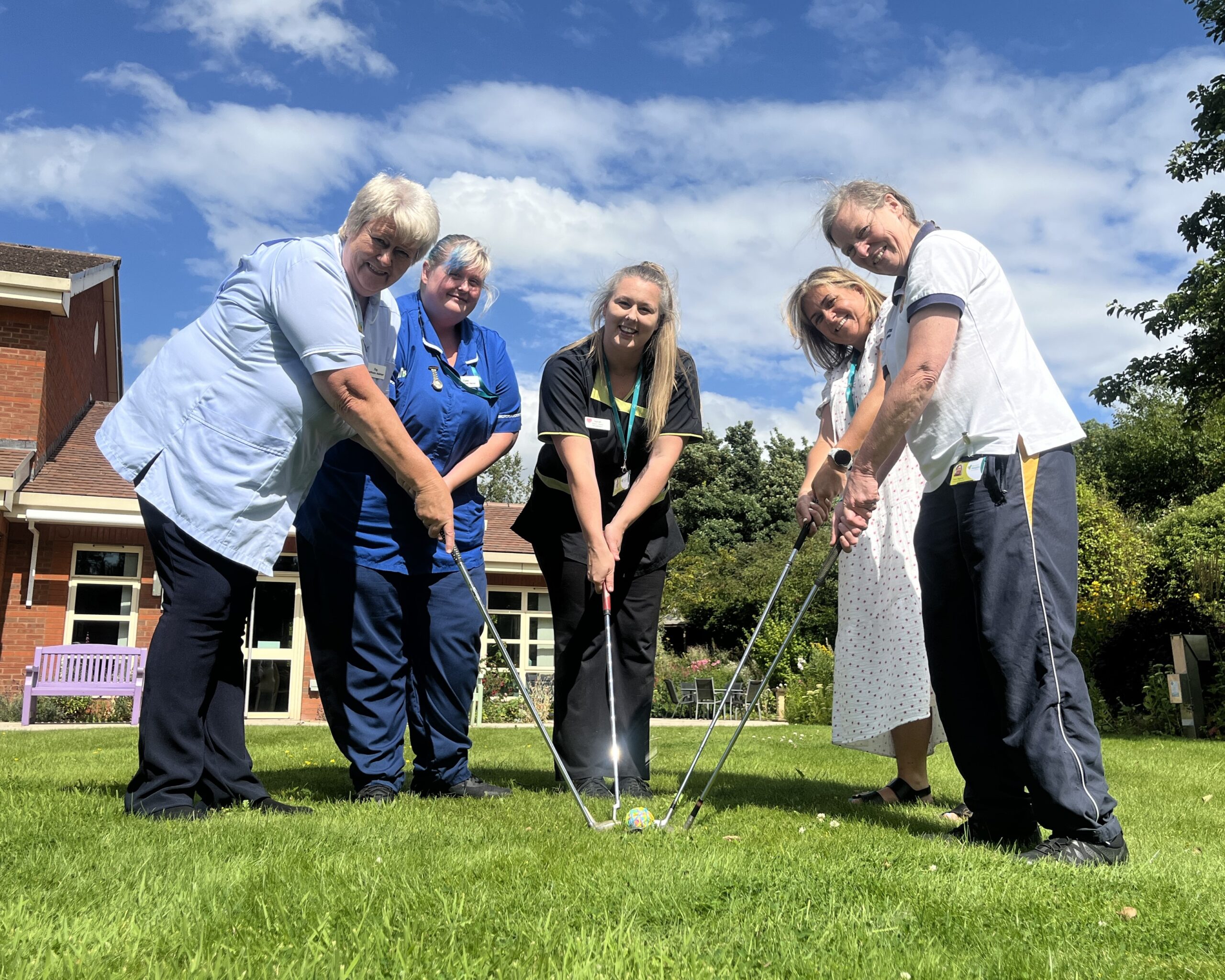 Five staff in nursing and housekeeping uniforms holding golf clubs