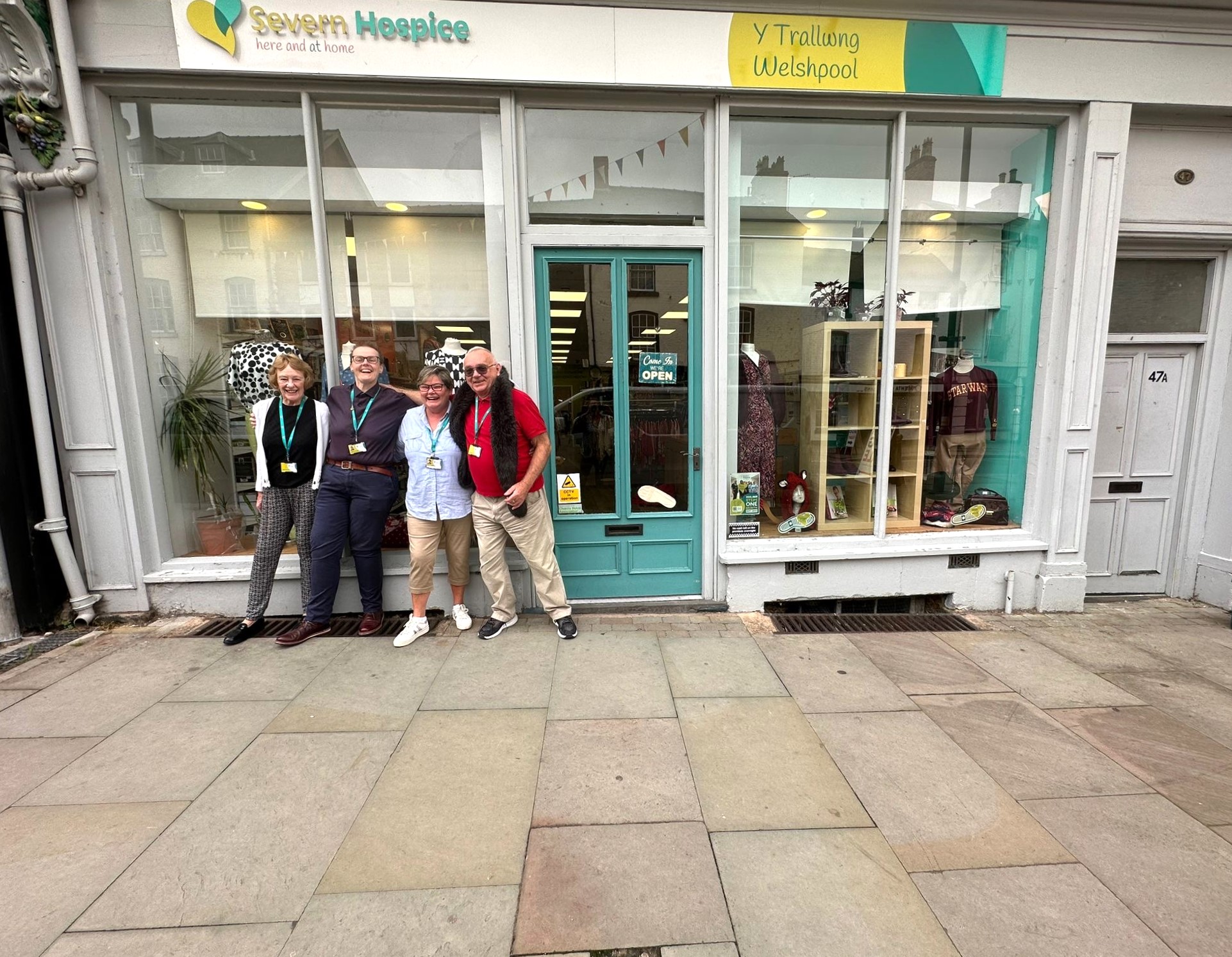 Welshpool shop staff and volunteers are laughing outside their shop.