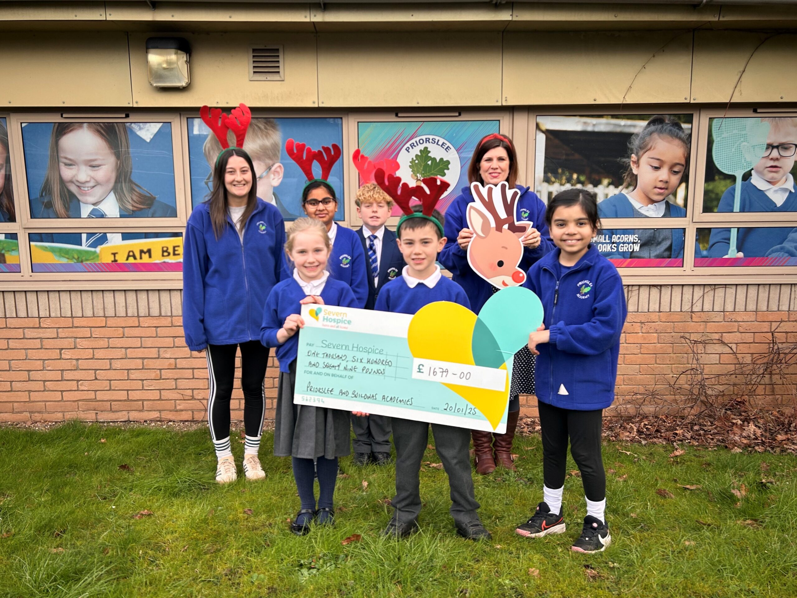 A group of children and their teacher pose wearing antlers and holding a cheque for £1679.