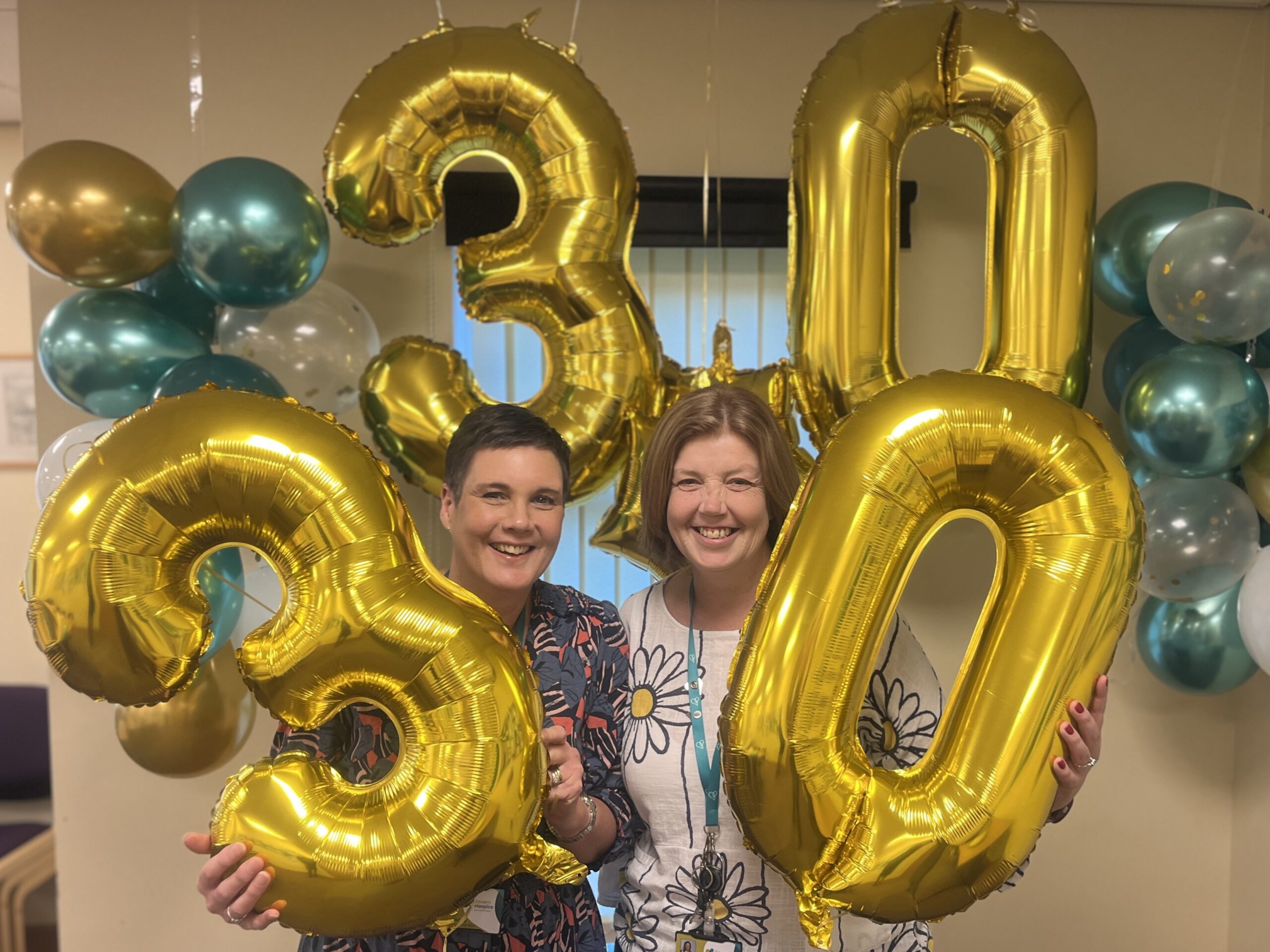 Two people holding huge gold balloons in the shape of a three and a zero